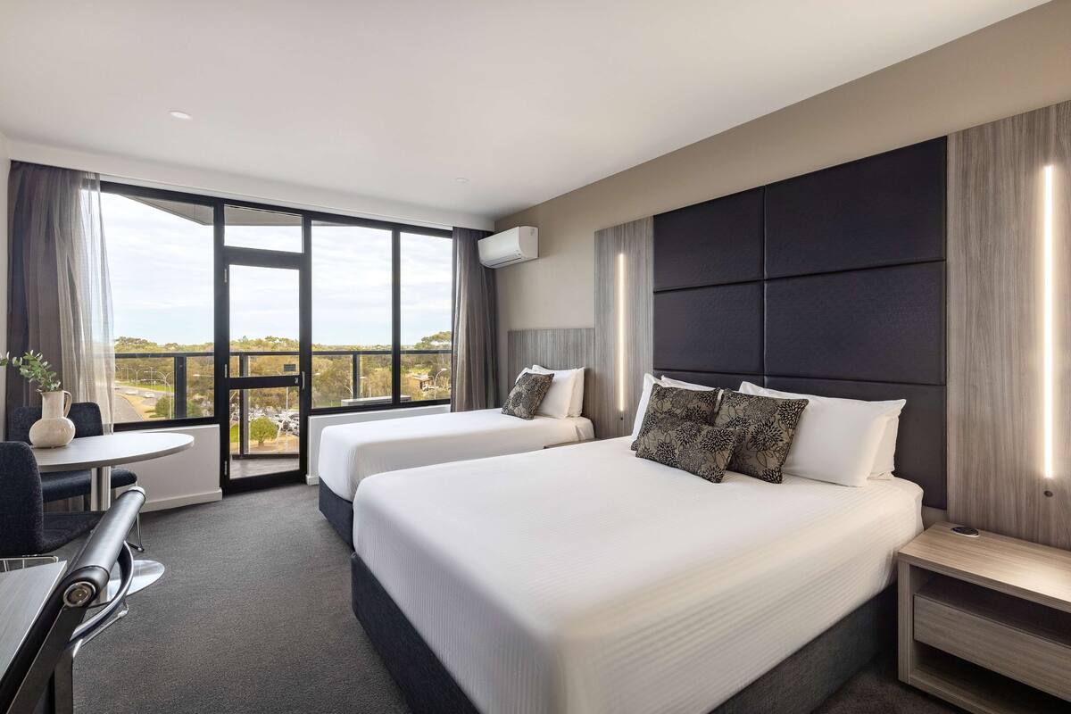 A hotel room with two beds, a desk, and a view of the city.