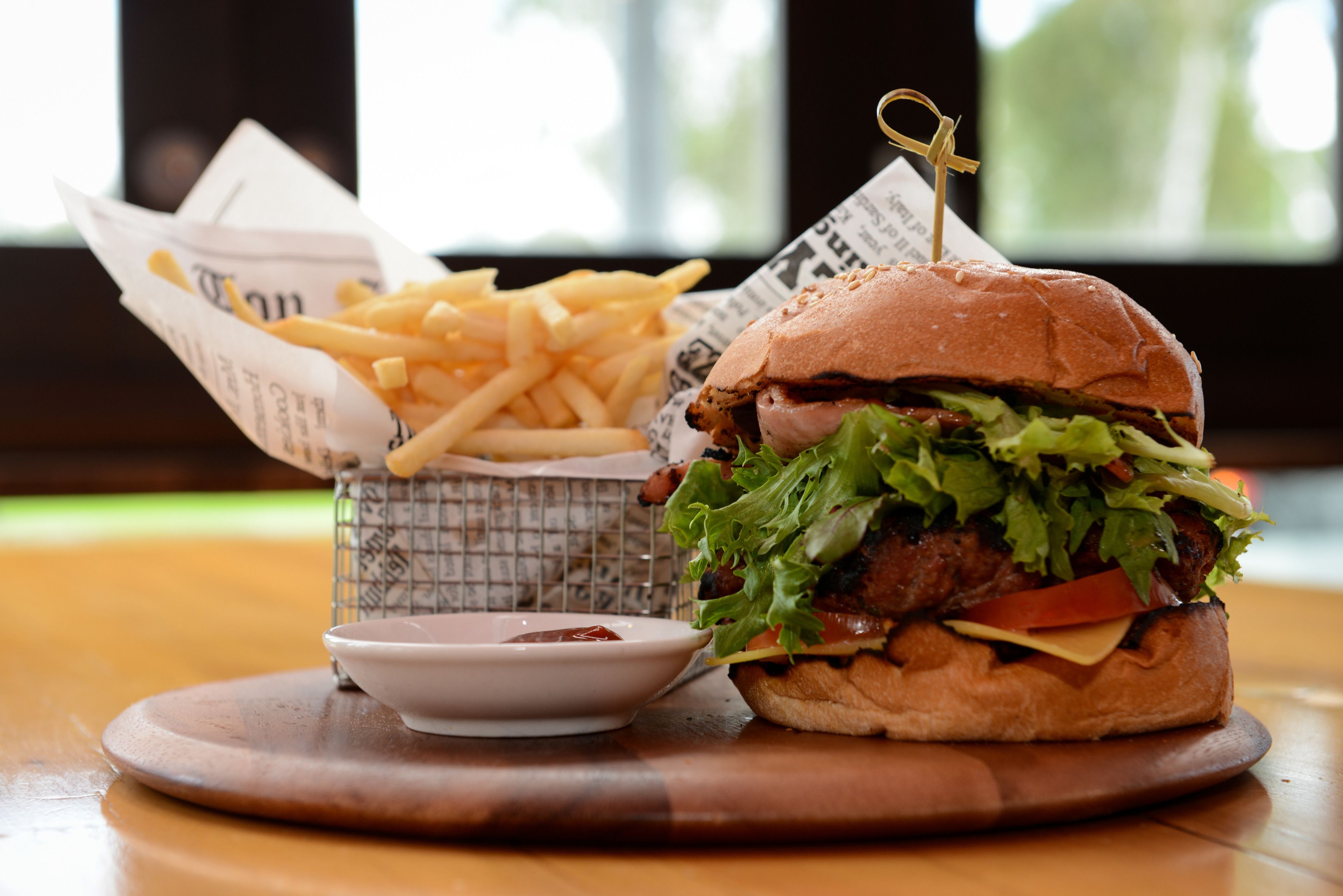 Un hamburger avec un cure-dent, des frites et un petit bol de ketchup sur une table en bois.