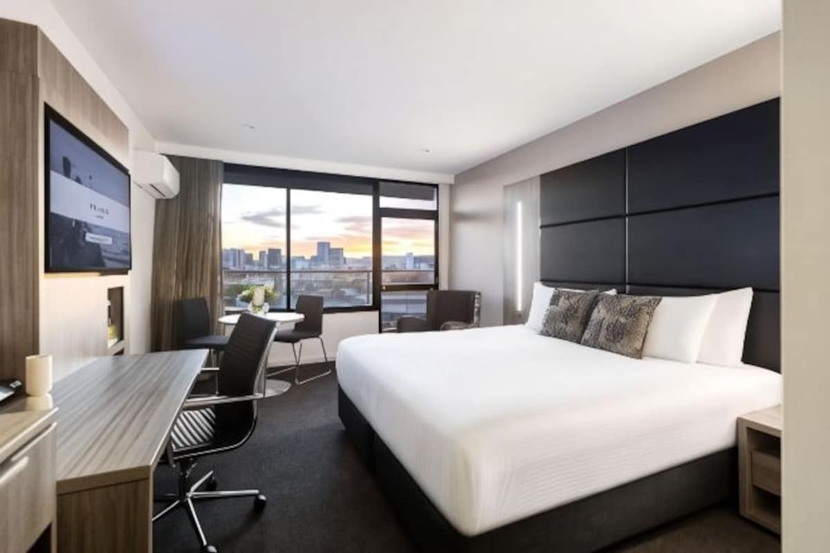 A modern hotel room with a large bed, a desk, and a city view.