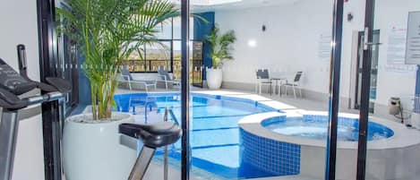 An indoor swimming pool with a hot tub, exercise equipment, and seating areas.
