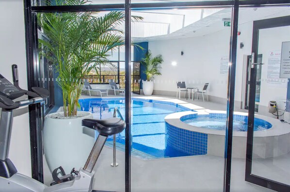 An indoor swimming pool with a hot tub, exercise equipment, and seating areas.