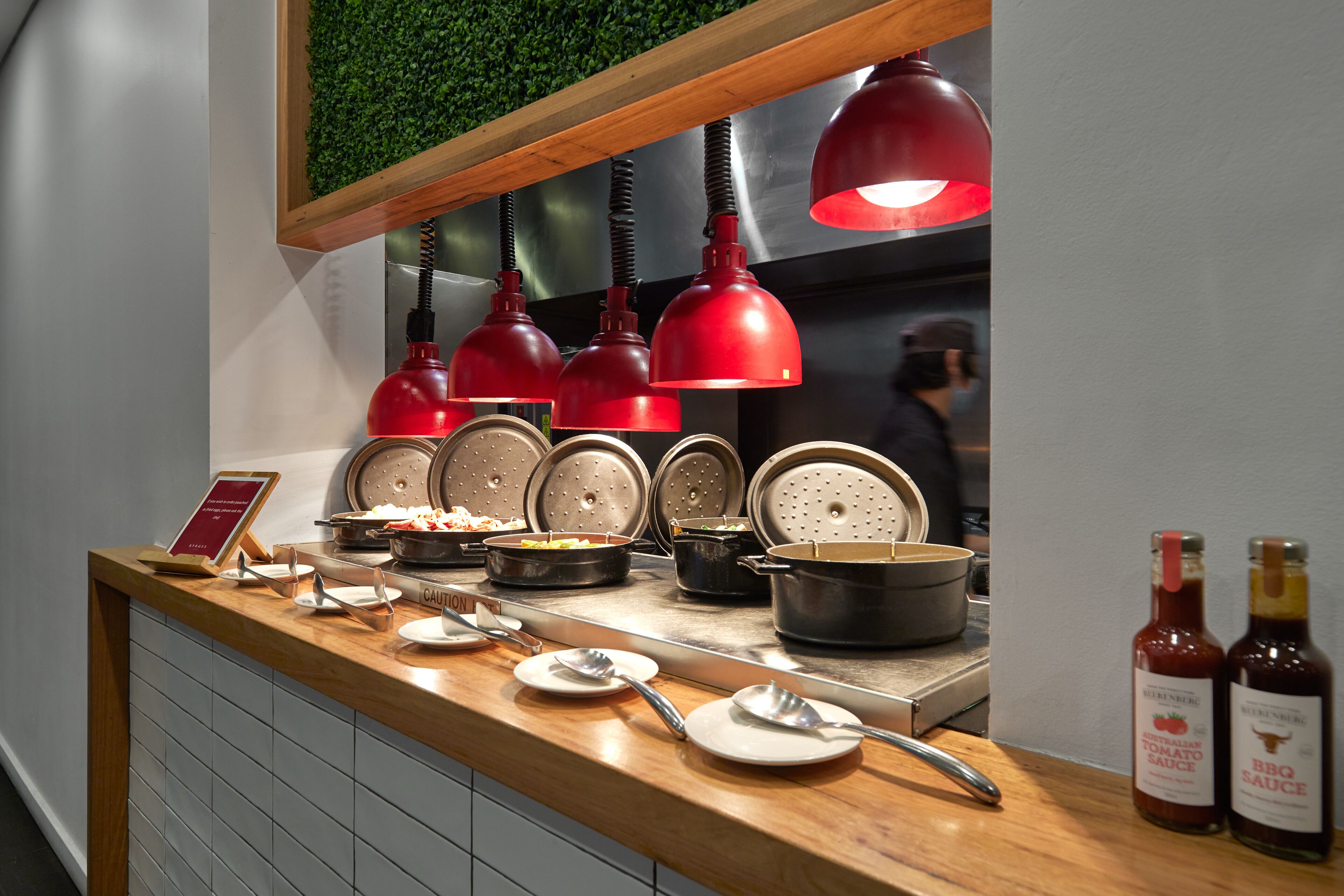Buffet com diversos alimentos, temperos, um letreiro, pratos, colheres e garrafas de molhos.