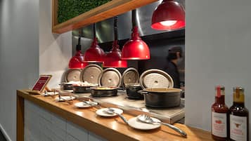 Buffet com diversos alimentos, temperos, um letreiro, pratos, colheres e garrafas de molhos.