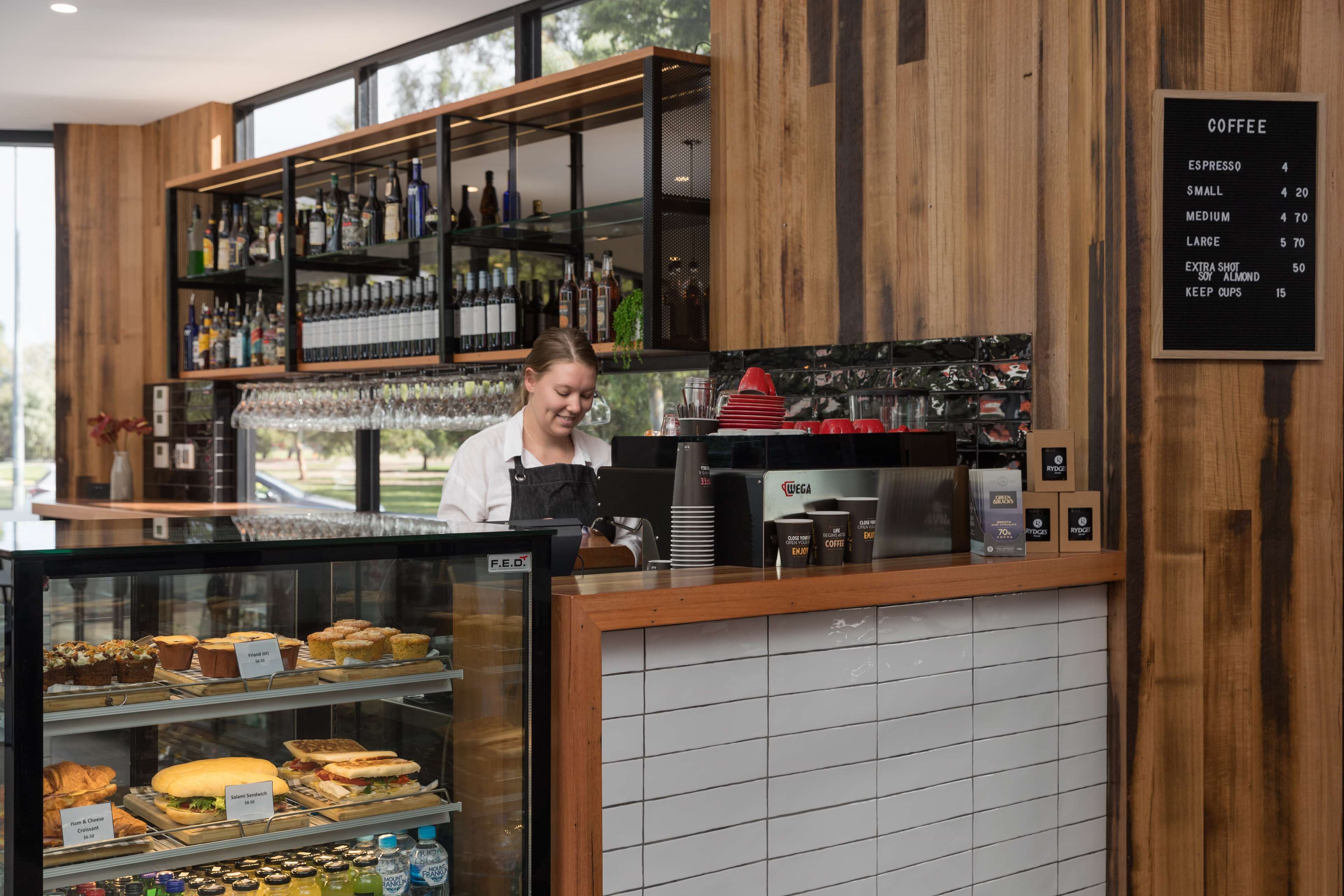 A coffee shop with a menu board, a display of pastries, and a bar area with various bottles.