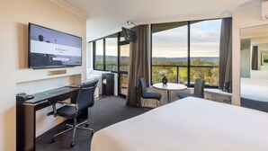 A hotel room with a large bed, a desk with a chair, a small table, and a TV mounted on the wall displaying a welcome screen. - Rydges South Park Adelaide (Adelaide)