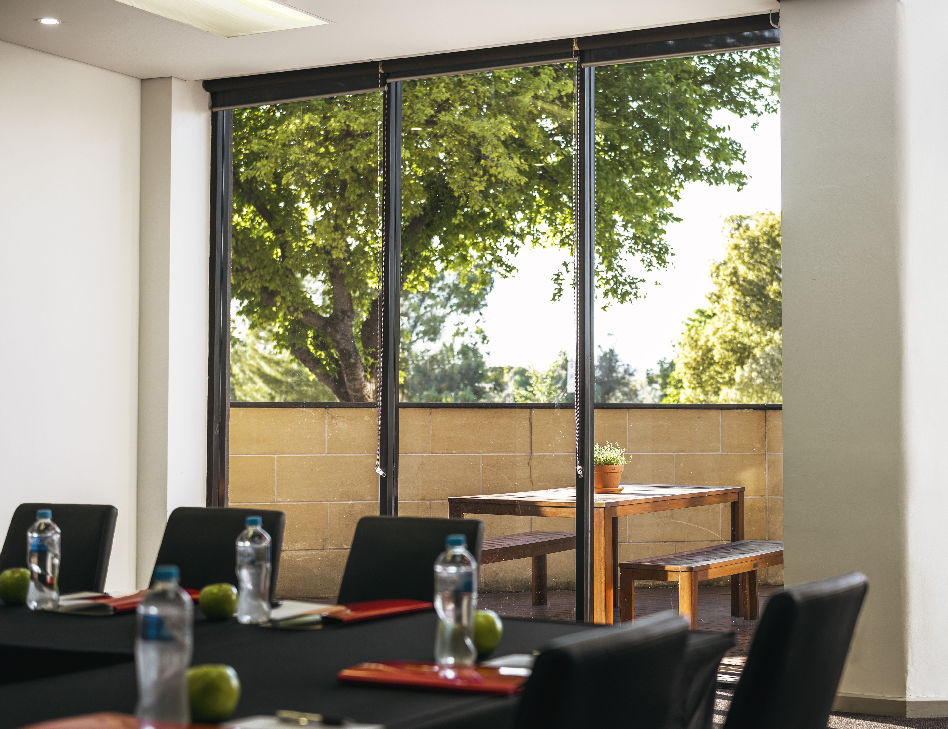 A conference room with a large window, a wooden table, and black chairs.