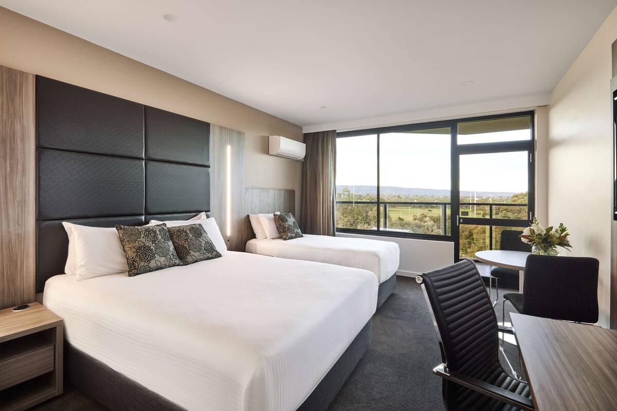 A hotel room with two beds, a desk, and a view of the outdoors.