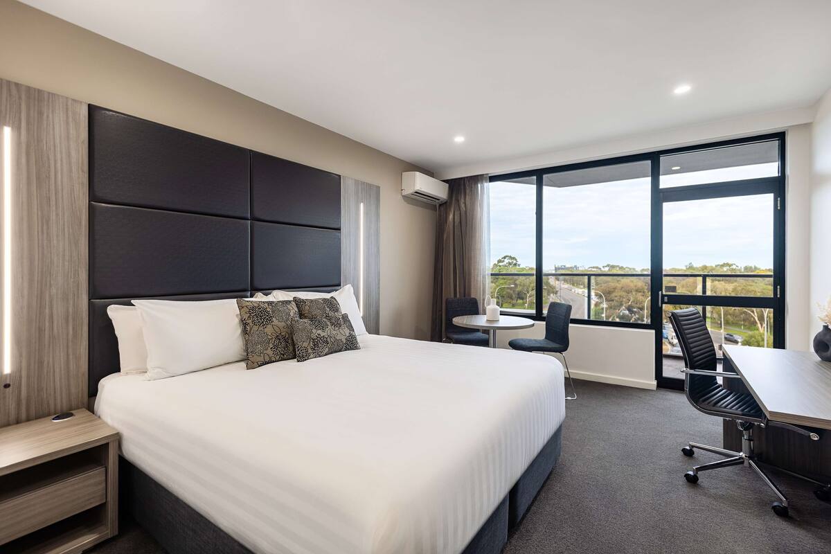 A modern hotel room with a large bed, a desk, and a view of the outdoors.