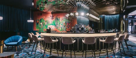 Zona de bar con una barra curva, varios taburetes y un mural llamativo en la pared.