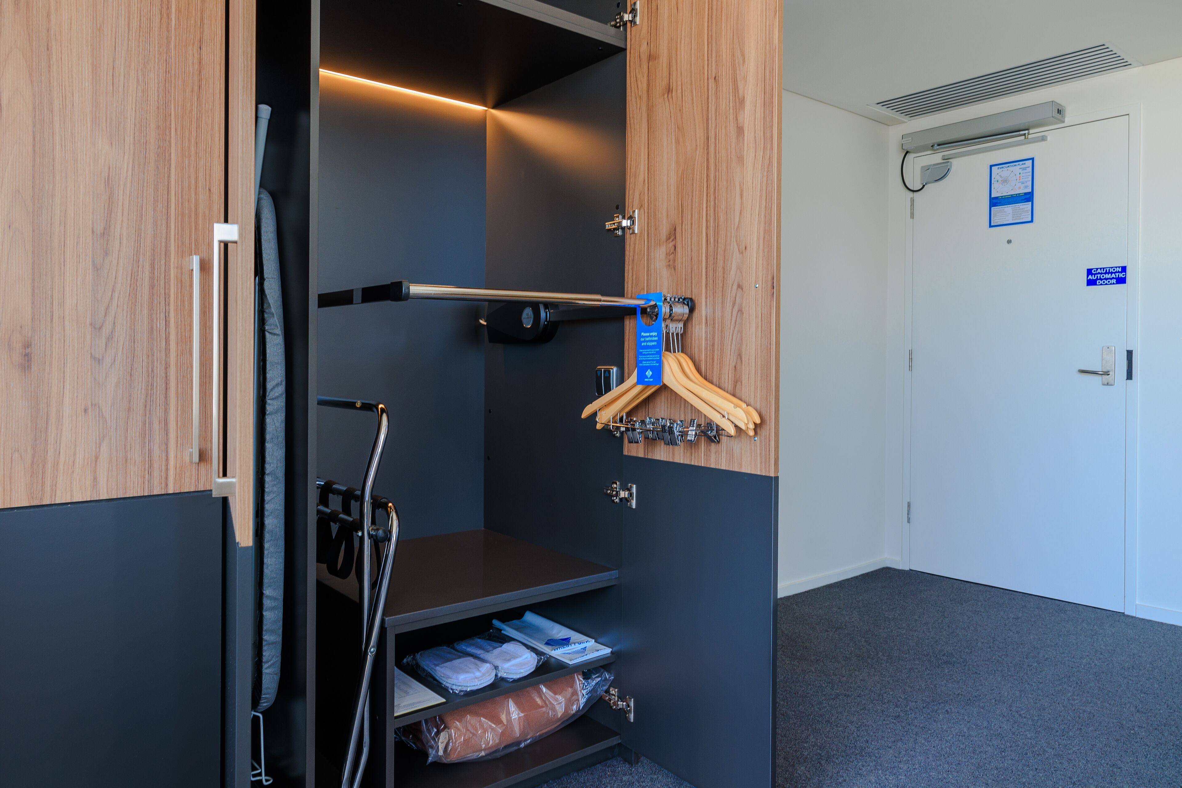 Habitación de hotel con armario de madera, perchero y estante con ropa doblada cuidadosamente.
