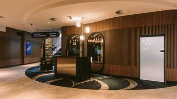 Vestíbulo de hotel con mostrador de recepción, escalera y señalización.