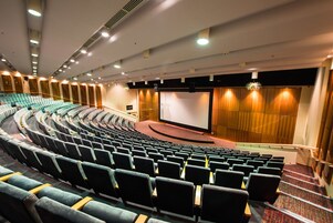 A theater with tiered seating, a large screen, and a stage.