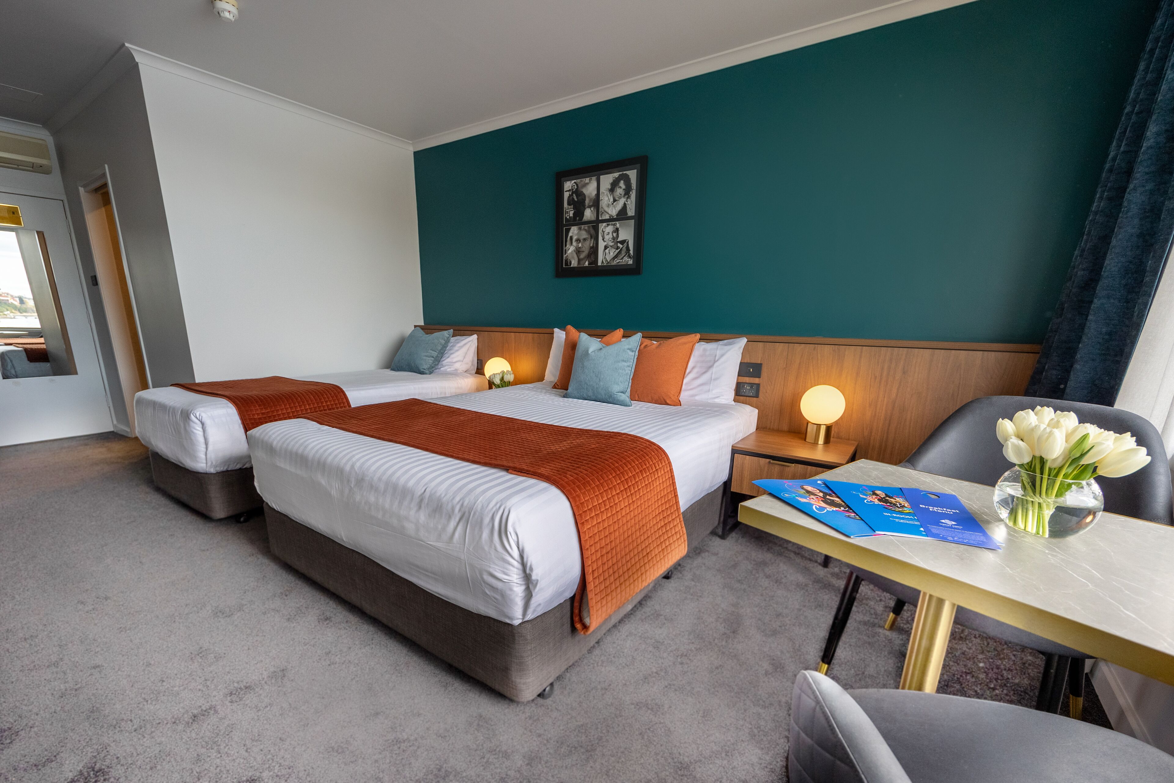 A hotel room with two beds, a desk with a lamp, and a chair.