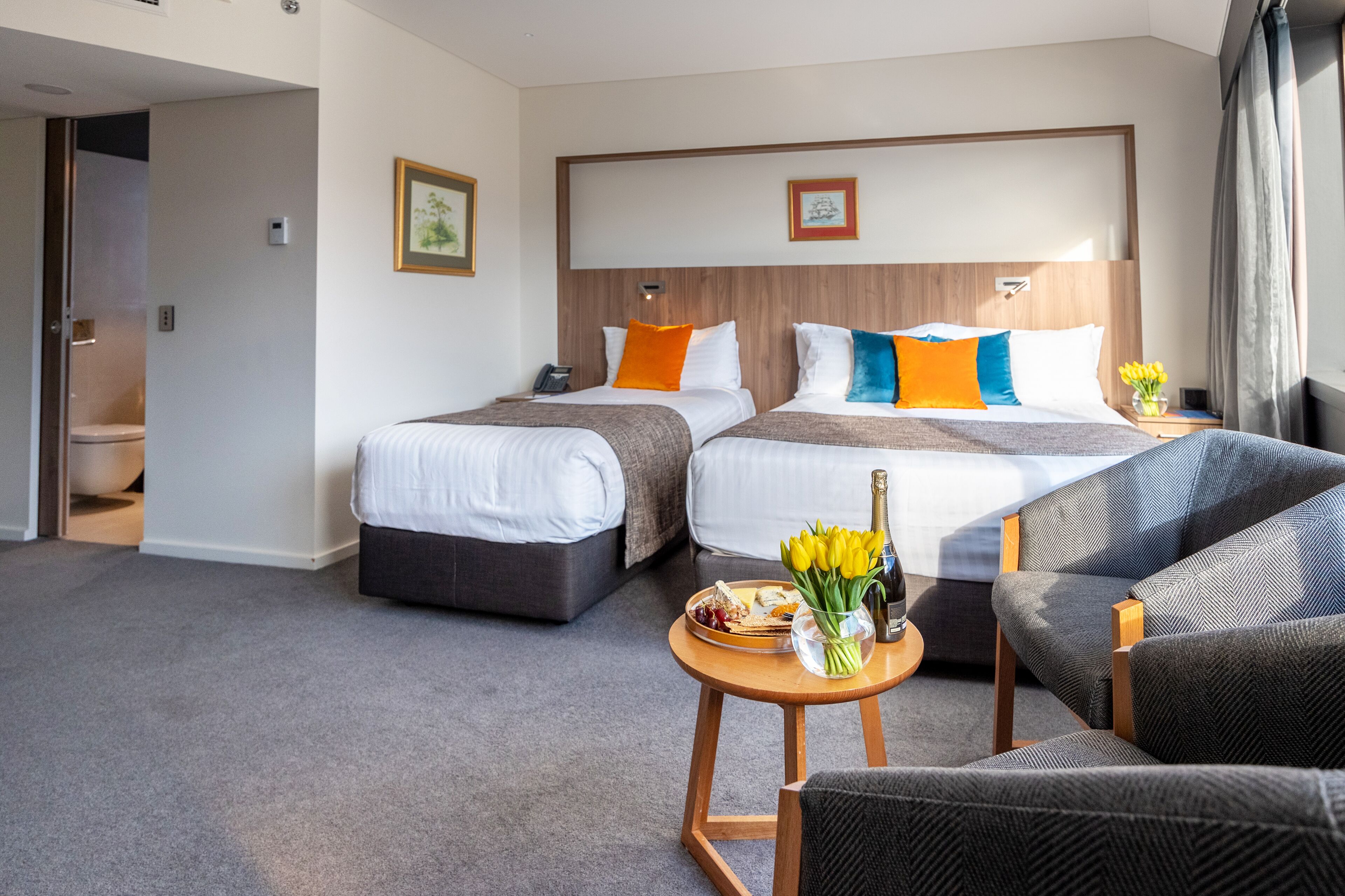 Habitación de hotel con dos camas, una zona de estar con mesa y vistas al exterior.