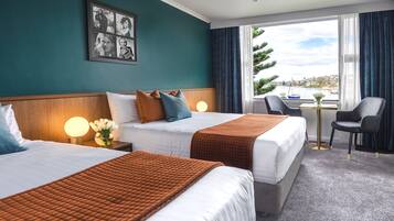 A hotel room with two beds, a small table, a chair, and a view of the sea.
