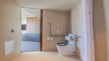 Un baño moderno con inodoro, ducha y puerta de cristal que da a una zona de cocina.