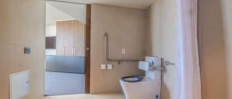 A modern bathroom with a toilet, shower, and a glass door leading to a kitchen area.