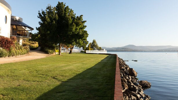 A waterfront property with a well-maintained lawn, a large tree, and a view of the water. - Wrest Point (Sandy Bay)