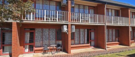 Un motel à deux étages, avec une façade en briques, de grandes fenêtres et un balcon à l’étage supérieur.
