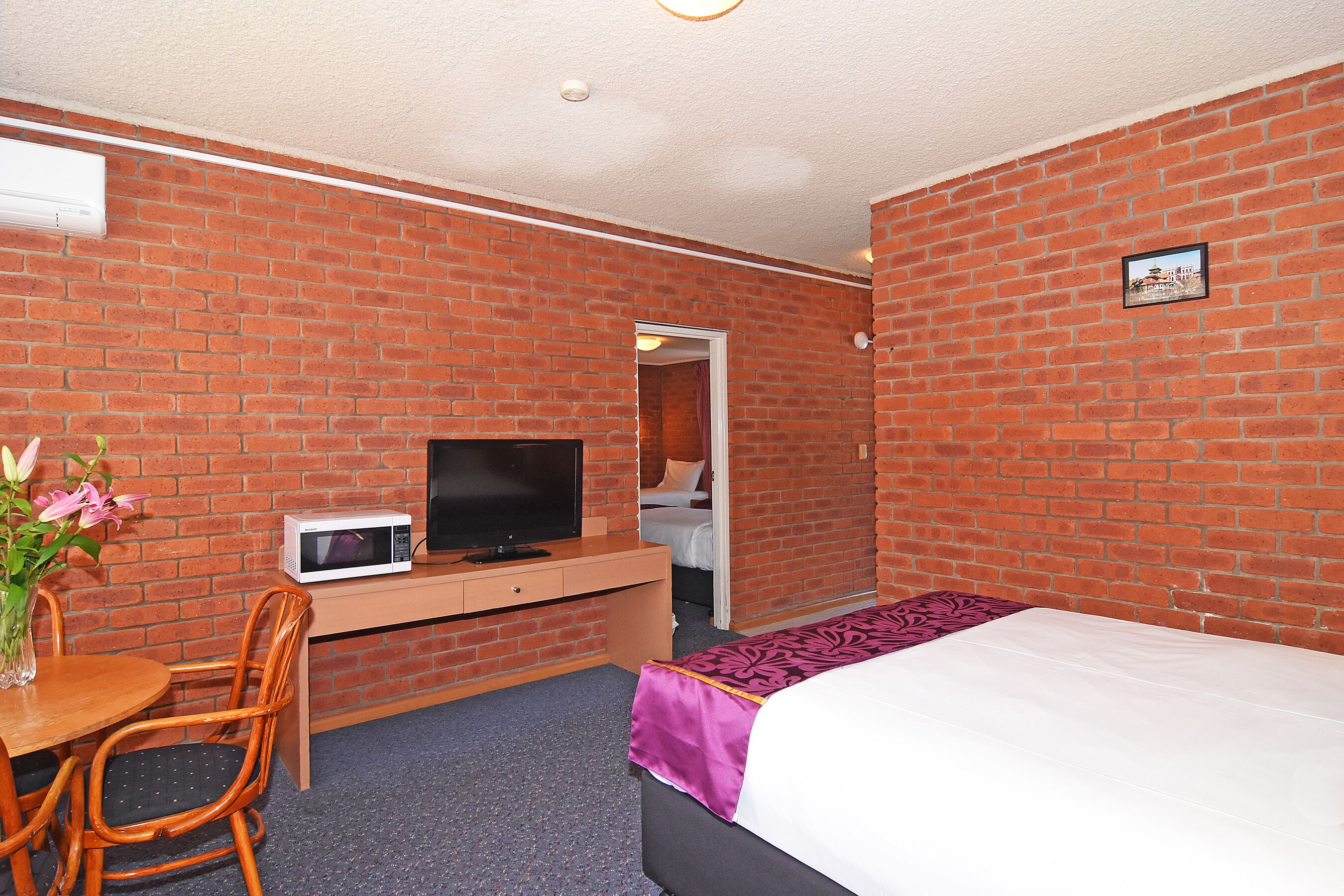 Habitación de hotel con pared de ladrillo, cama, escritorio con televisor y una silla.