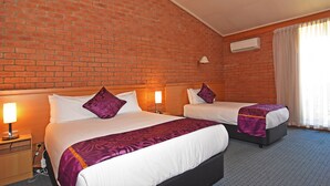 A hotel room with two beds, a brick wall, an air conditioning unit, and a window with curtains.
