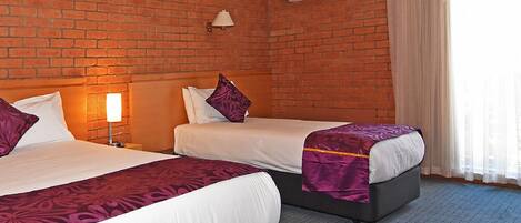 Habitación de hotel con dos camas, una pared de ladrillo, un equipo de aire acondicionado y una ventana con cortinas.