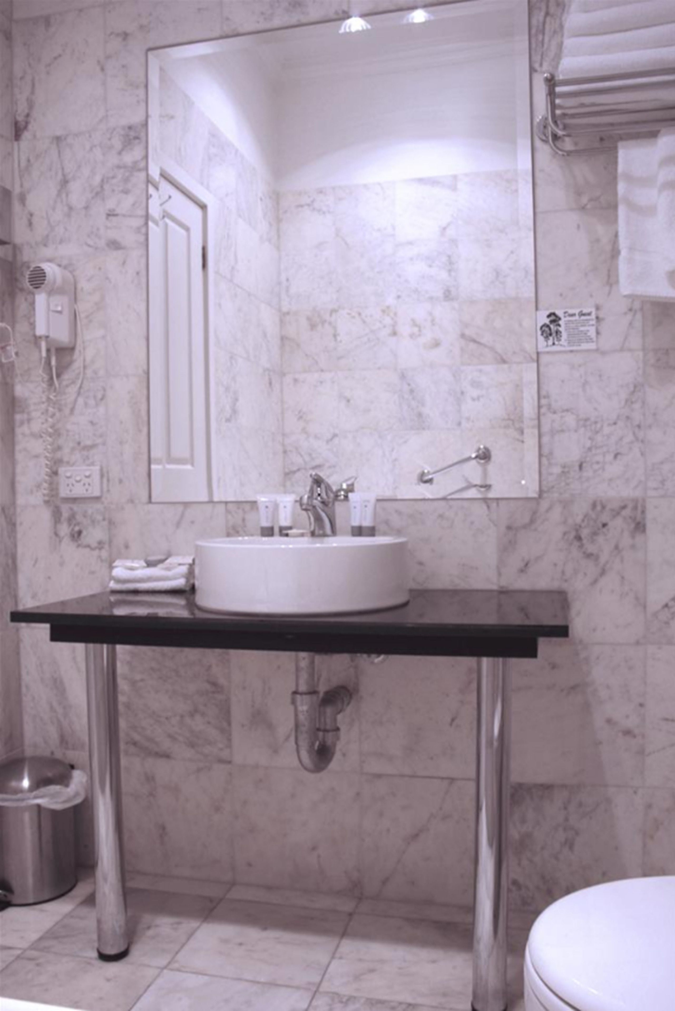 Ein modernes Badezimmer mit Marmorwand, einem großen Spiegel, einem weißen Waschbecken und einer Toilette.