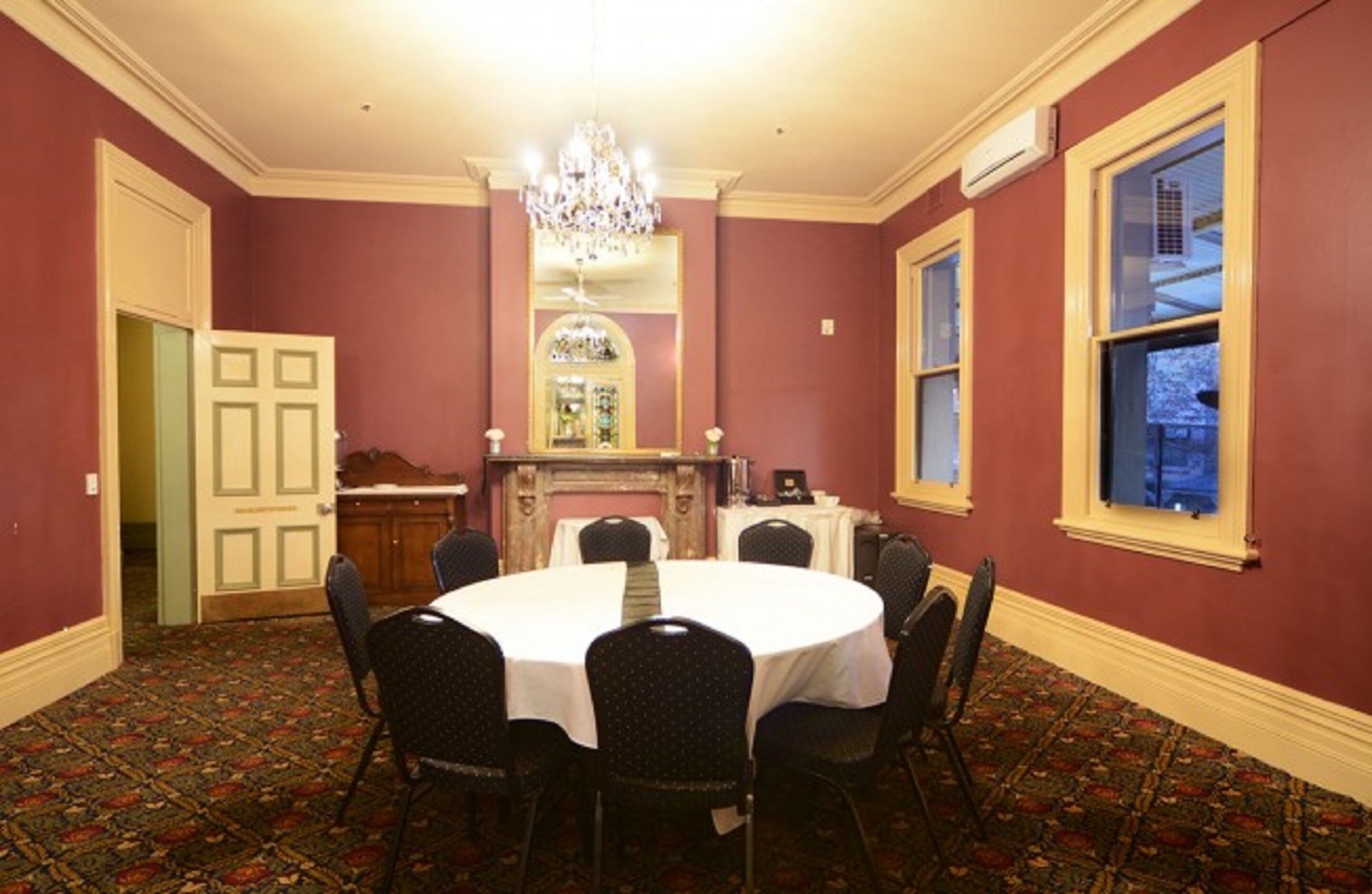 Une salle de conférence avec une table ronde, des chaises, un lustre, une cheminée et une vue par la fenêtre.