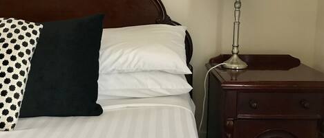 A neatly made bed with striped bedding, a dark wooden nightstand with a lamp, and a patterned pillow.
