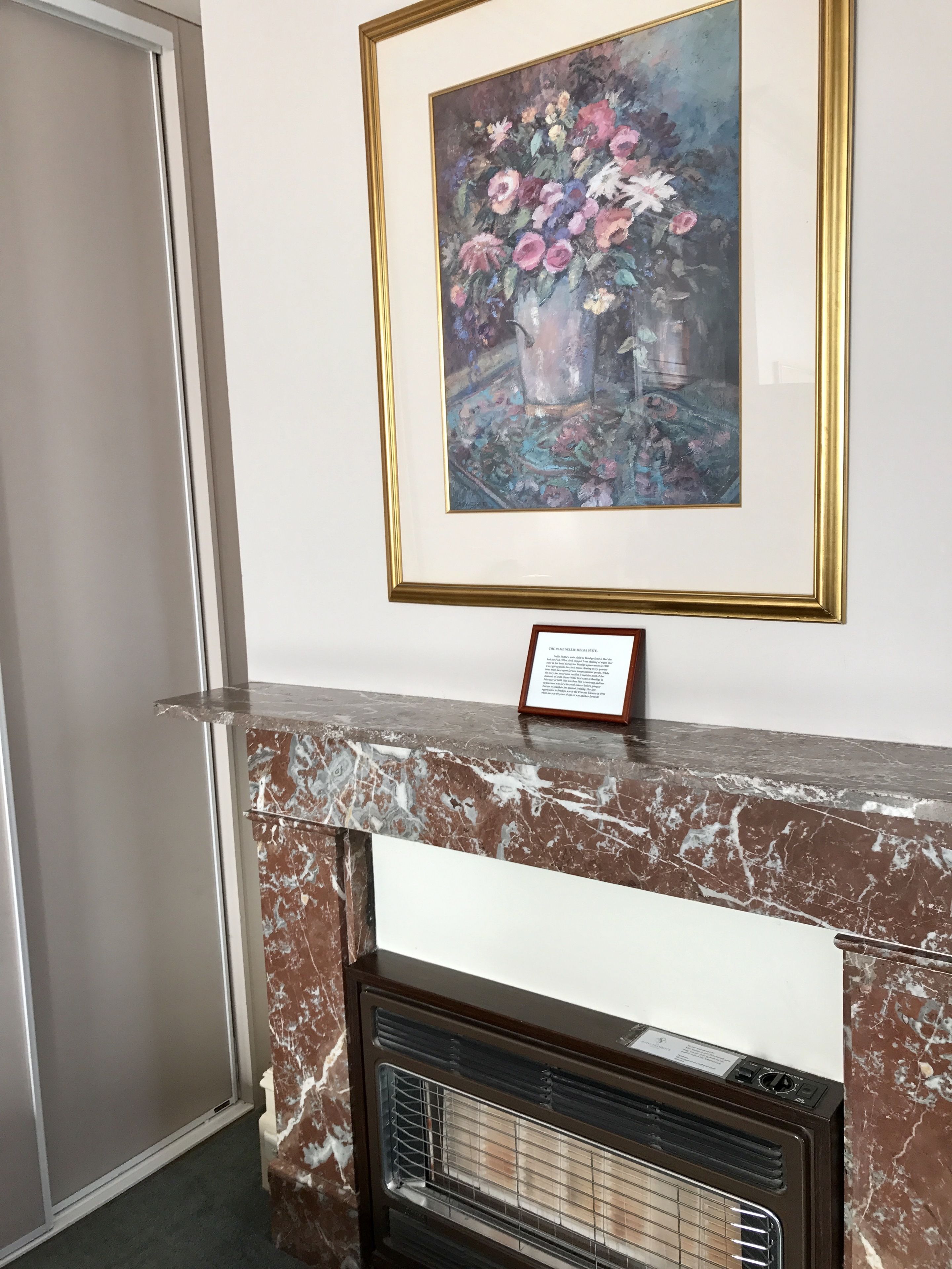 A marble fireplace with a framed painting of flowers above it.