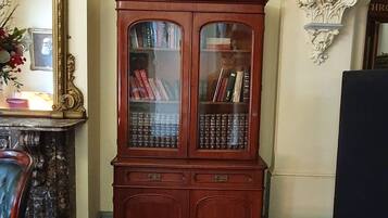 A room with a patterned carpet, a wooden cabinet with glass doors, a framed picture on the wall, and a large mirror.