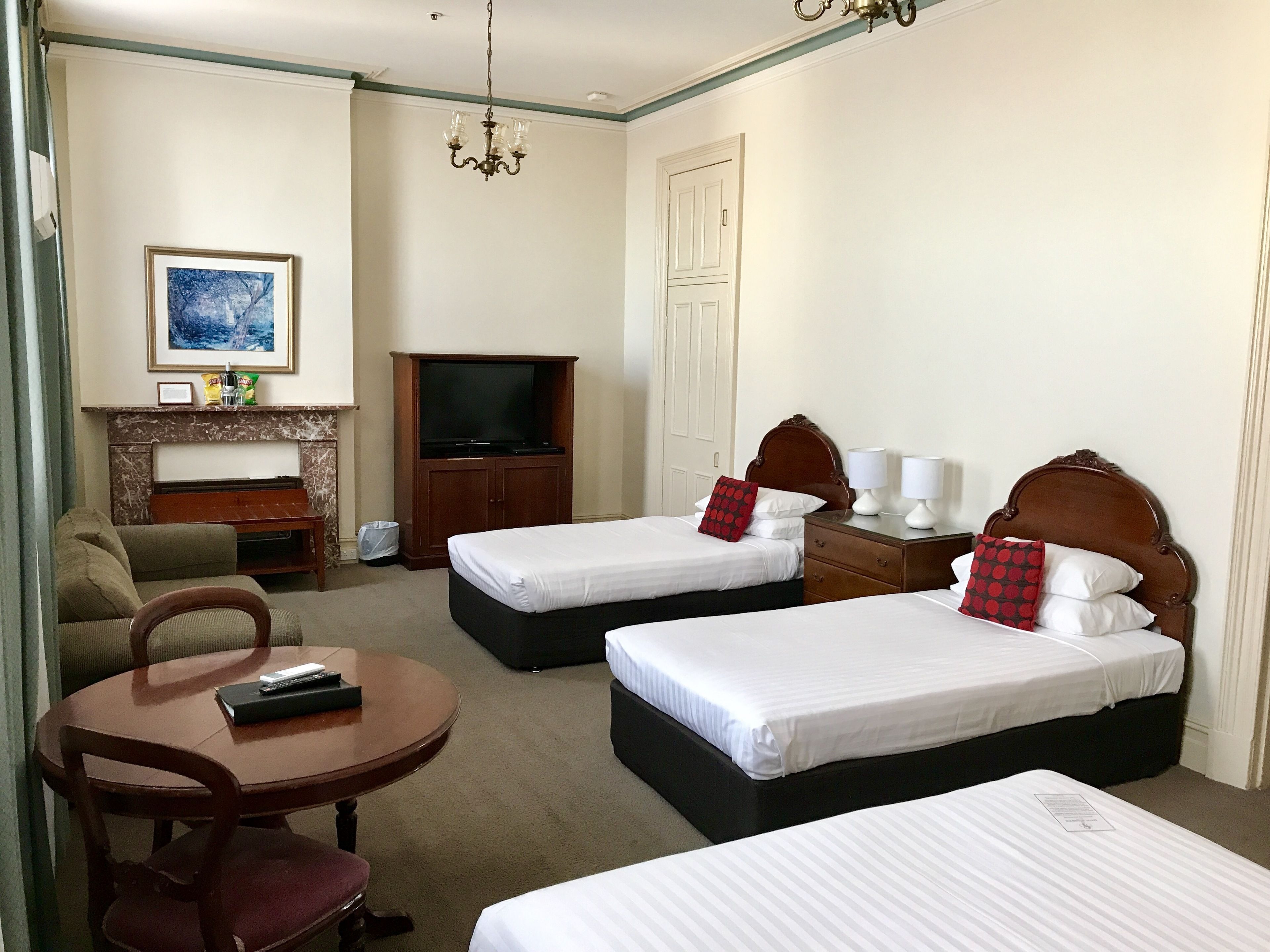 Habitación de hotel con dos camas individuales, un sofá, una mesita, televisión y chimenea.
