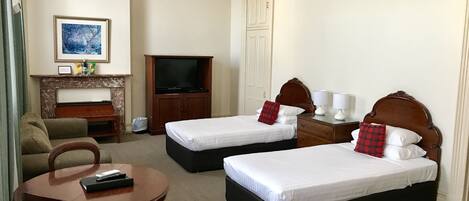 Habitación de hotel con dos camas individuales, un sofá, una mesita, televisión y chimenea.