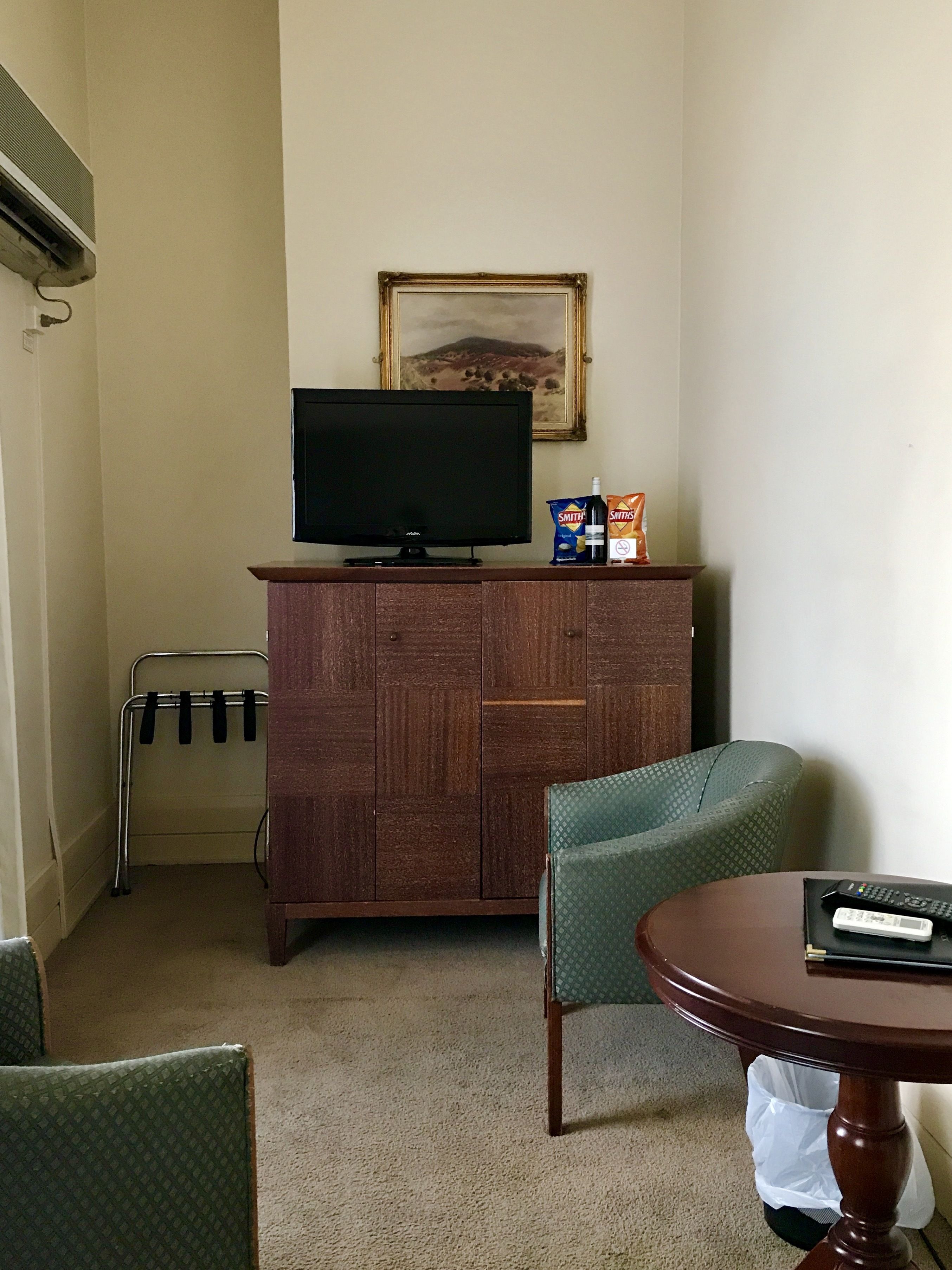 Ein Hotelzimmer mit Holzschrank, Fernseher, einem Gemälde an der Wand, einem Sessel und einem Tisch mit Fernbedienung.