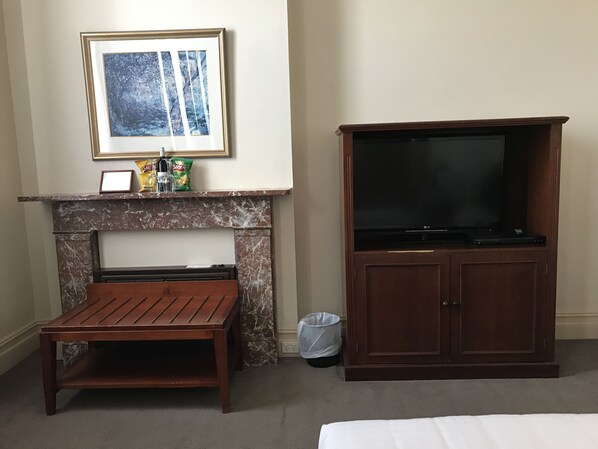 Una habitación con chimenea, un televisor sobre un mueble, una pequeña mesa de madera y un cuadro enmarcado en la pared.