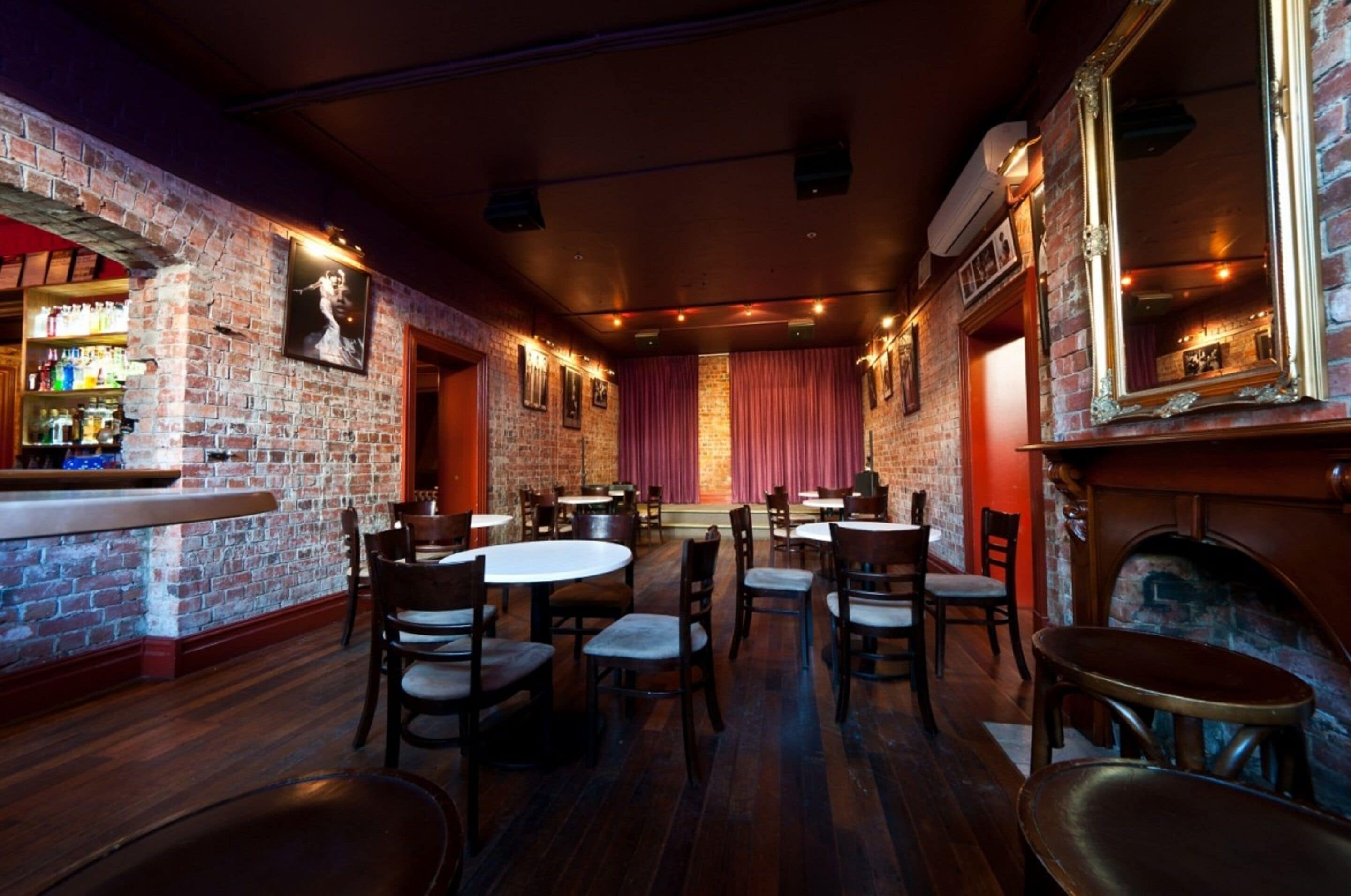 A brick-walled bar area with tables and chairs, a fireplace, and a mirror on the wall.