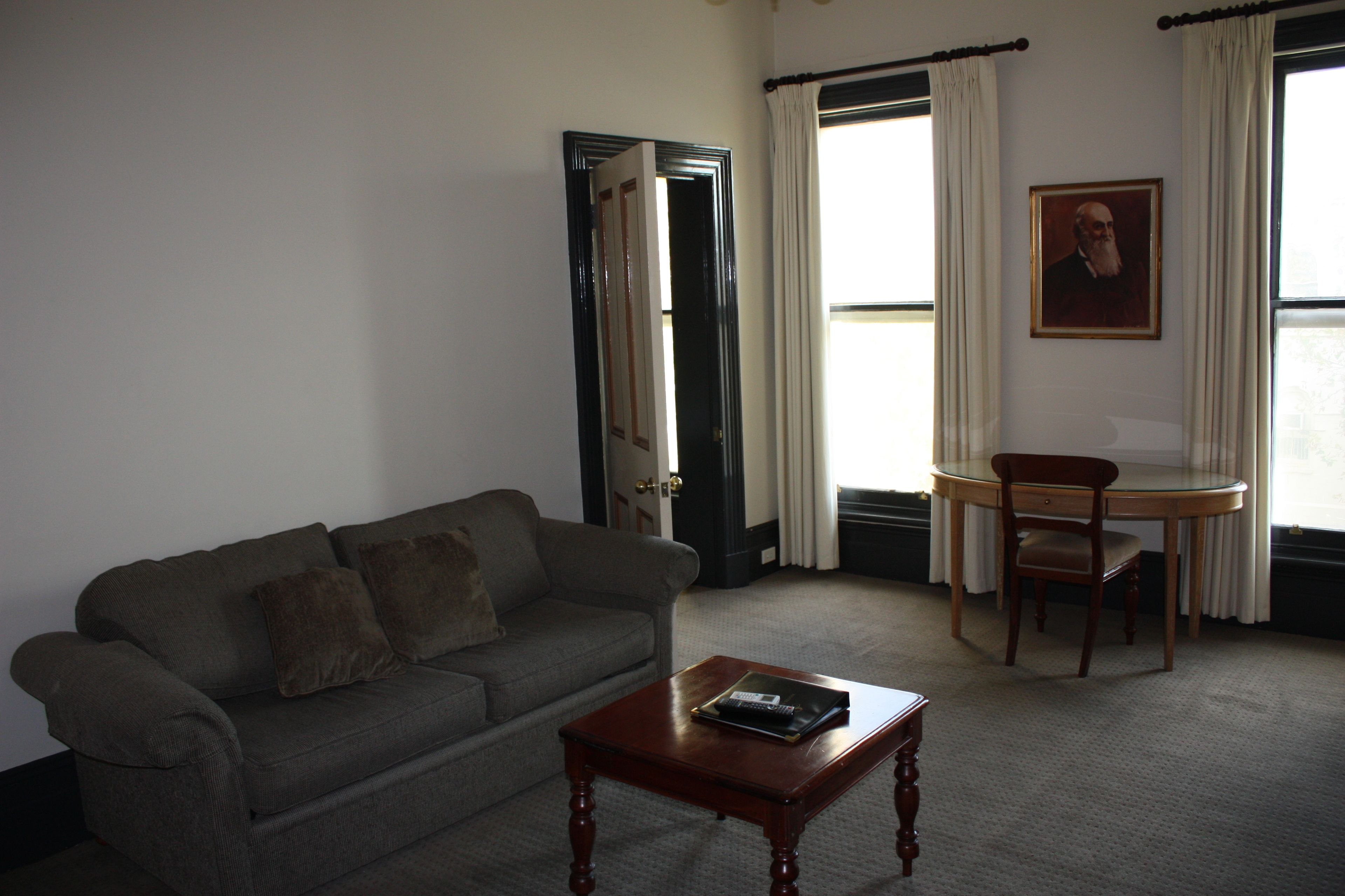 A living room with a sofa, a coffee table, a dining table with a chair, and a framed portrait on the wall.
