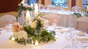 En festlig banket med borde dækket til en formel begivenhed, med blomsterarrangementer, stearinlys og glas.