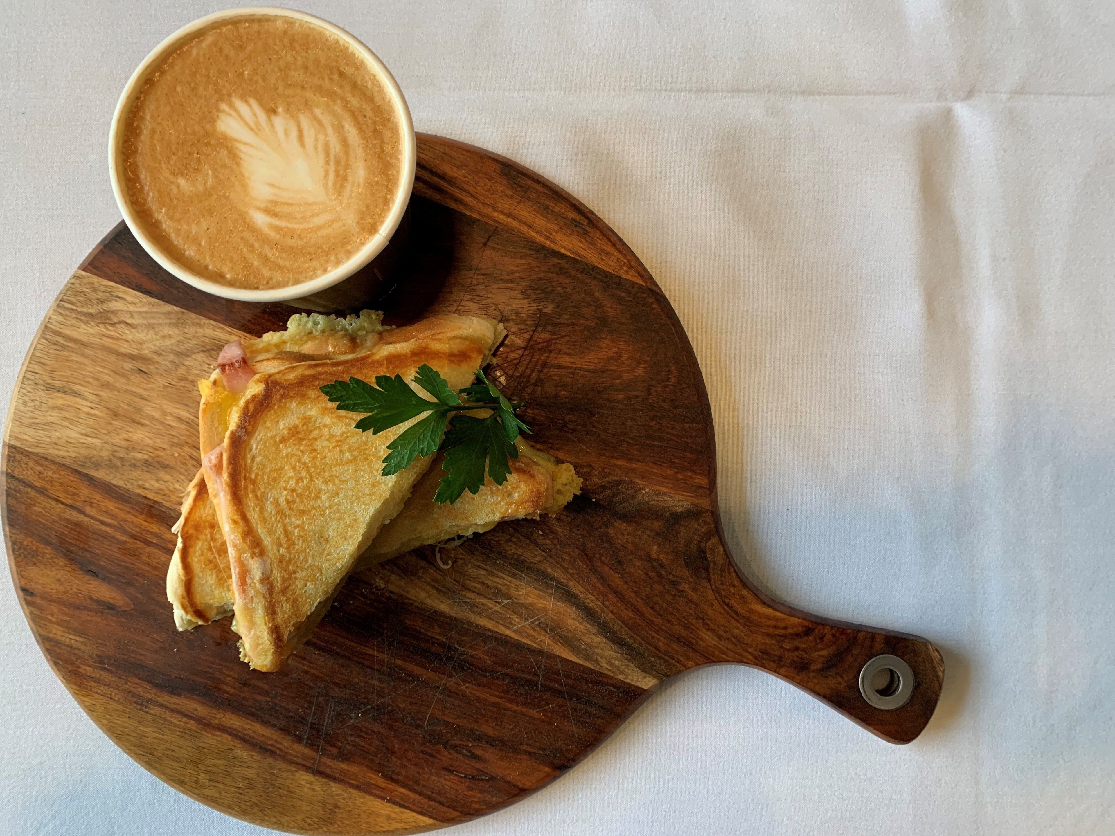 A sandwich on a wooden board with a cup of coffee beside it.
