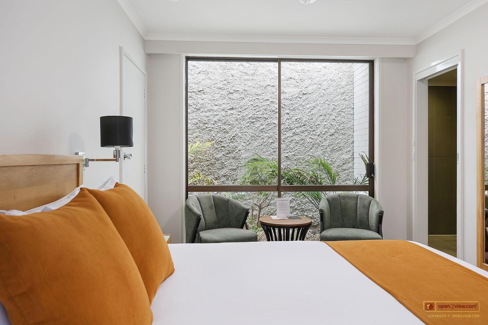 A hotel room with a large bed, two armchairs, a small table, and a TV mounted on the wall.