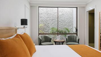 A hotel room with a large bed, two armchairs, a small table, and a TV mounted on the wall.