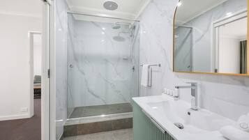 Un baño moderno con ducha de mampara de vidrio, un lavabo blanco con gabinete verde y un espejo grande con marco dorado.