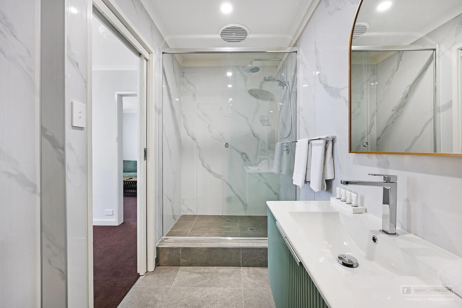 Een moderne badkamer met een douche in een glazen cabine, een wit marmeren wastafelmeubel en een grote spiegel.