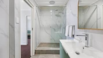 Een moderne badkamer met een douche in een glazen cabine, een wit marmeren wastafelmeubel en een grote spiegel.