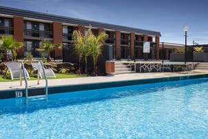 Una piscina con sillones de descanso y un edificio con varios balcones al fondo.