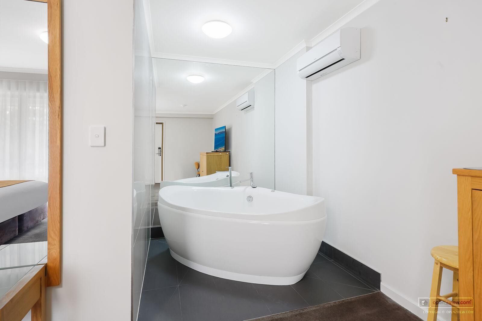 Een moderne badkamer met een vrijstaand bad, een spiegel en een houten kruk.