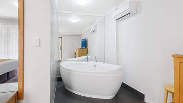 Een moderne badkamer met een vrijstaand bad, een spiegel en een houten kruk.