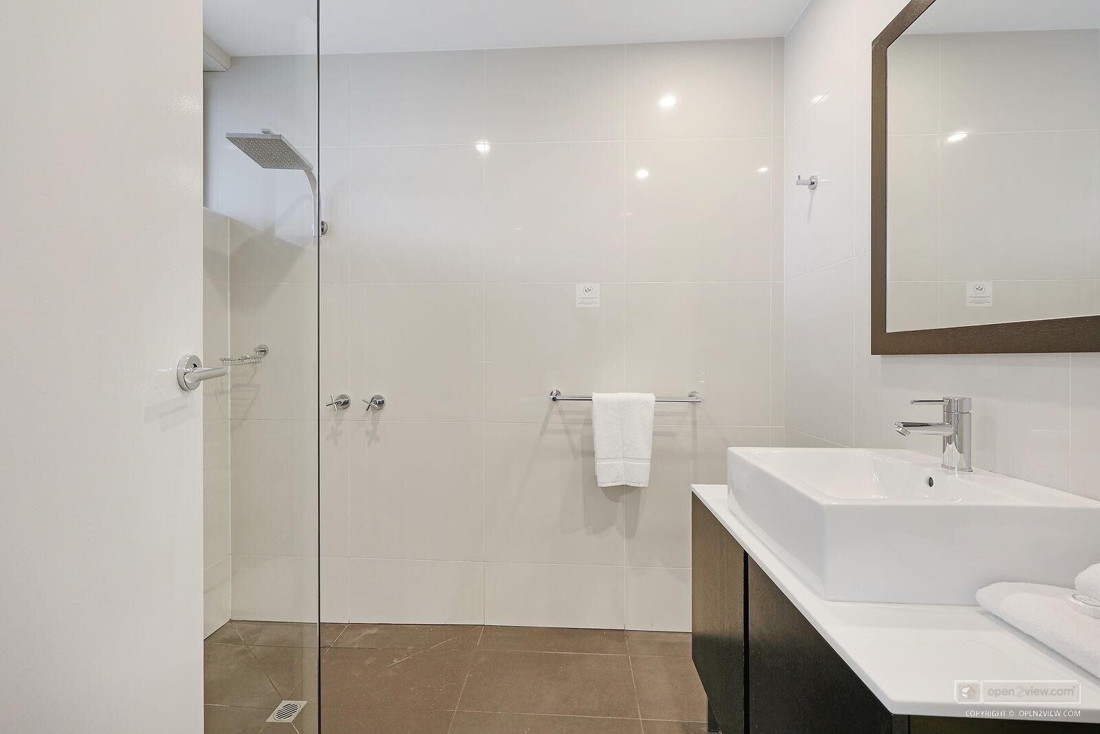 A modern bathroom with a glass-enclosed shower, a white sink, and a large mirror.