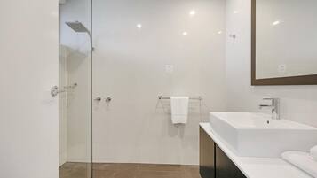 A modern bathroom with a glass-enclosed shower, a white sink, and a large mirror.