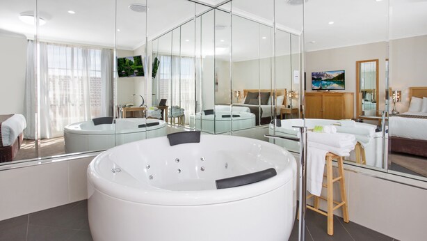 Un baño moderno con una bañera blanca grande, un taburete de madera y un espejo que refleja la habitación.